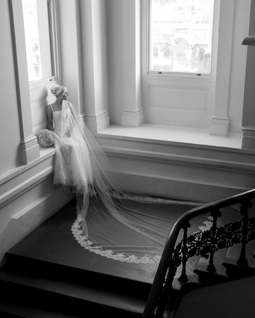 a bride with her long veil looks out the window at the immigration museum outside The Trust in Melbourne